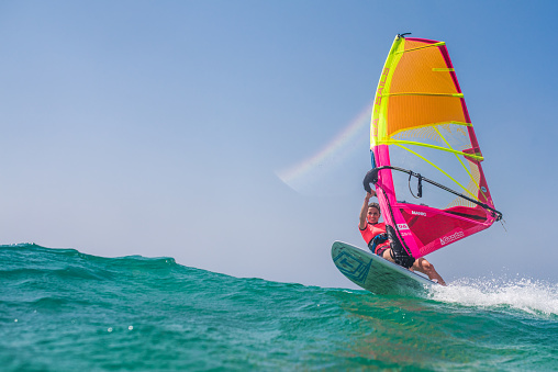 Young woman windsurfing on sea with board and colourful sail.