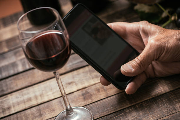 Wine app Man tasting a glass of red wine and using apps on his smartphone, wine culture and technology concept winery photos stock pictures, royalty-free photos & images