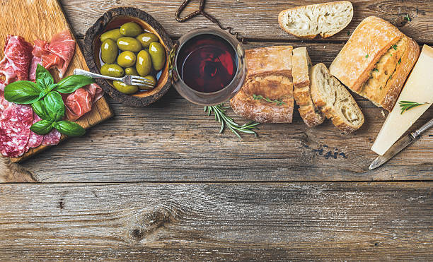 Wine snack set and glass of red over wooden background Wine snack set. Glass of red wine, green mediterranean olives, prosciutto, salami and aged cheese over rustic wooden background. Top view, copy space, horizontal composition antipasto stock pictures, royalty-free photos & images