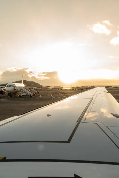 Wing of a plane in the foreground on the runway with a plane in the background ready to board at sunset stock photo