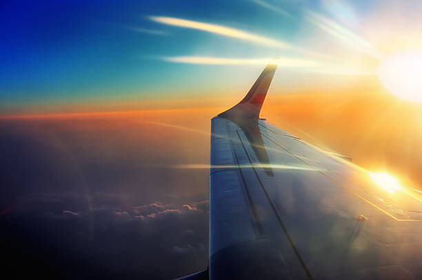 wing of the airplane in flight in sunrise beams stock photo