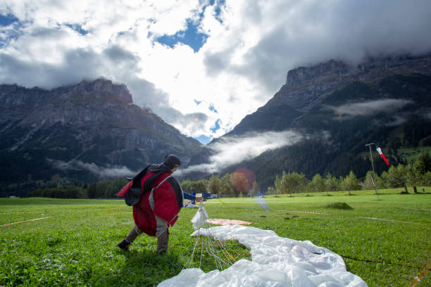 Wing suit flier comes into landing on grassy field in the morning He flies down into valley to meet friends in the Swiss Alps base jumping stock pictures, royalty-free photos & images