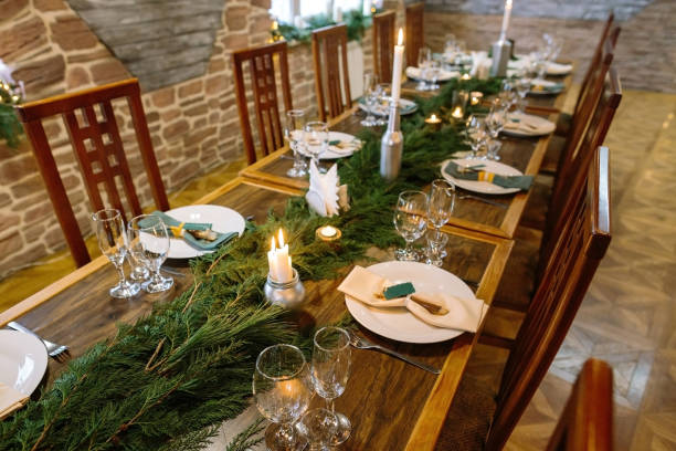 winter, atmosphere, celebration concept. in the dining room there is an elegant furniture made of natural materials, long table served and decorated with branches of spruce and candles stock photo