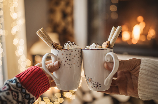 Lazy winter day in front of fire in fireplace. Woman and man hands with a cup of hot chocolate.