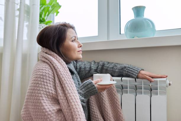 Winter season, woman warming up near home heating radiator stock photo