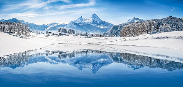 Winter wonderland in the Alps reflecting in crystal-clear mountain lake Panoramic view of beautiful white winter wonderland scenery in the Alps with snowy mountain summits reflecting in crystal clear mountain lake on a cold sunny day with blue sky and clouds. european alps stock pictures, royalty-free photos & images