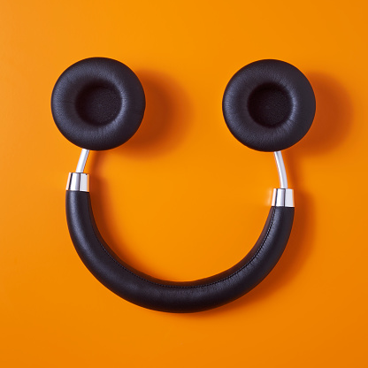 high angle view of a pair of black wireless full size headphones upside down on an orange background, resembling a smiley face