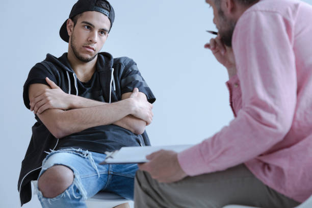 A withdrawn rebel young boy with behavioral and social disorders during his individual meeting with a psychotherapist. A withdrawn rebel young boy with behavioral and social disorders during his individual meeting with a psychotherapist. gang stock pictures, royalty-free photos & images