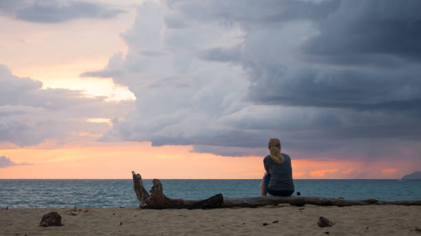 A womam is Sitting on a beach in Puerto Rico, watching the sunset and the arrival of a storm over the Caribbean Sea. Rincon, Puerto Rico, USA. A womam is Sitting on a beach in Puerto Rico, watching the sunset and the arrival of a storm over the Caribbean Sea. Rincon, Puerto Rico, USA. puerto rican women stock pictures, royalty-free photos & images