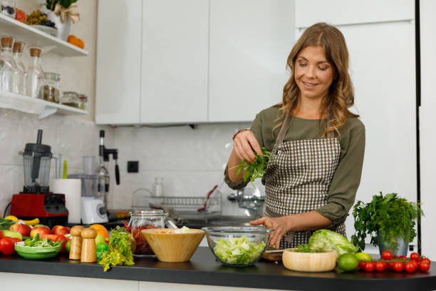 Woman adding a handful of arugula to a salad she is preparing stock photo