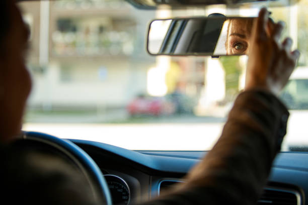 Woman adjusting her rear view mirror before driving Over the shoulder view of elegant mature woman sitting in driver's seat in her car and adjusting the rear view mirror before driving. rear view mirror stock pictures, royalty-free photos & images