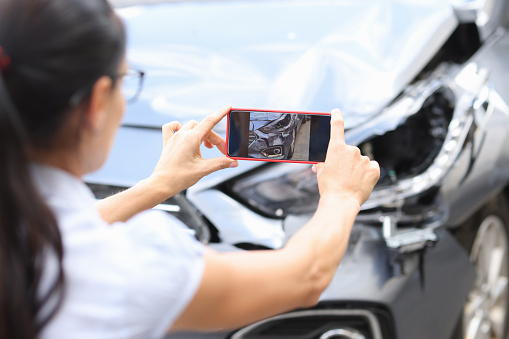Woman agent takes pictures of damage to car after accident by smartphone. Consequences of car accident concept
