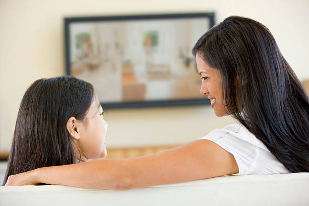 Woman and girl in living room with flat screen television Woman and young girl in living room with flat screen television sitting on sofa chatting to each other asian kids watching tv stock pictures, royalty-free photos & images