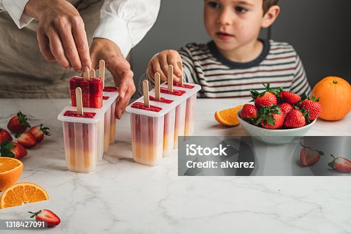 istock Woman and son making orange and strawberry ice pops 1318427091