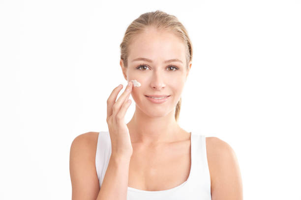 Woman applying face cream Beautiful young woman applying face cream and looking at camera while standing at isolated white background. applying face cream stock pictures, royalty-free photos & images