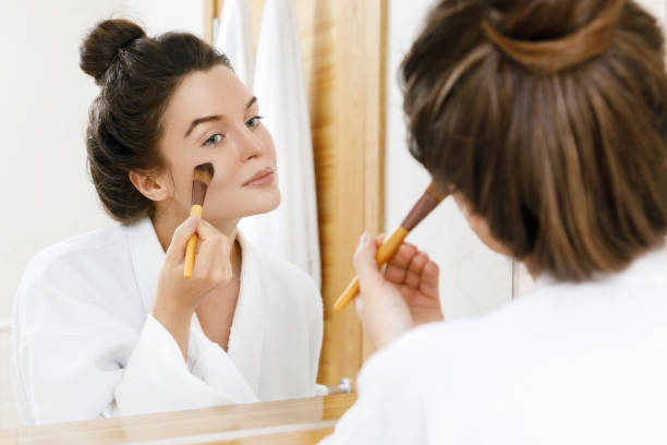 Woman applying foundation or blusher on her face Woman looking in the mirror and applying foundation or blusher on her face applying blush stock pictures, royalty-free photos & images