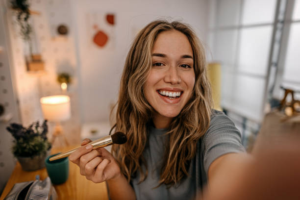 Woman applying make-up with brush and recording vlog Portrait of smiling young women applying make-up on face with brush and recording vlog and taking selfie for social media skincare technology stock pictures, royalty-free photos & images