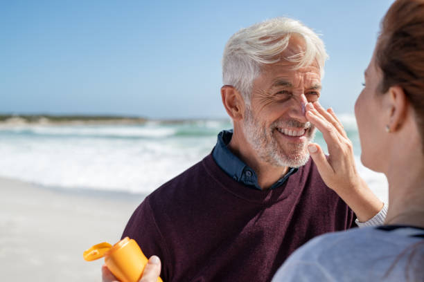 Woman applying sunscreen on senior man nose Portrait of cheerful old man looking at his mature wife applying sunscreen on nose. Senior husband enjoying vacation with woman while applying sunscreen on face at beach. Middle aged retired couple applying suntan lotion at sea with copy space. sunscreen stock pictures, royalty-free photos & images