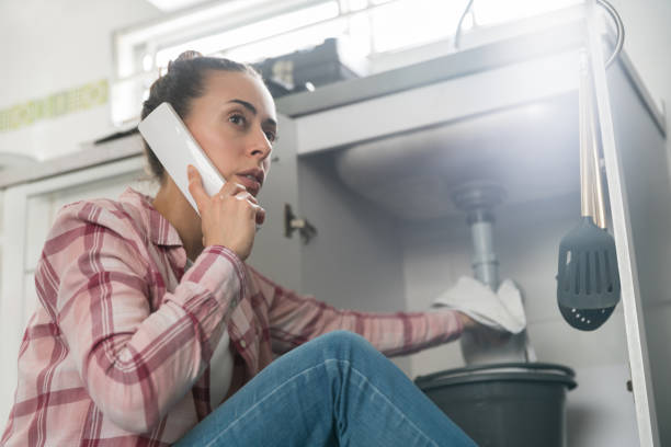 Woman at home calling a plumber about a leaking pipe in her sink Latin American woman at home calling a plumber about a leaking pipe in her sink and looking very worried water pipe stock pictures, royalty-free photos & images