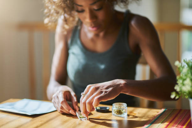 woman at home rolling marijuana joint from dispensary bought weed african american woman at home rolling marijuana joint from dispensary bought weed marijuana joint stock pictures, royalty-free photos & images