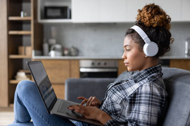 Woman at home working on her laptop and using headphones Young African American woman working on her laptop at home and using headphones streaming service stock pictures, royalty-free photos & images