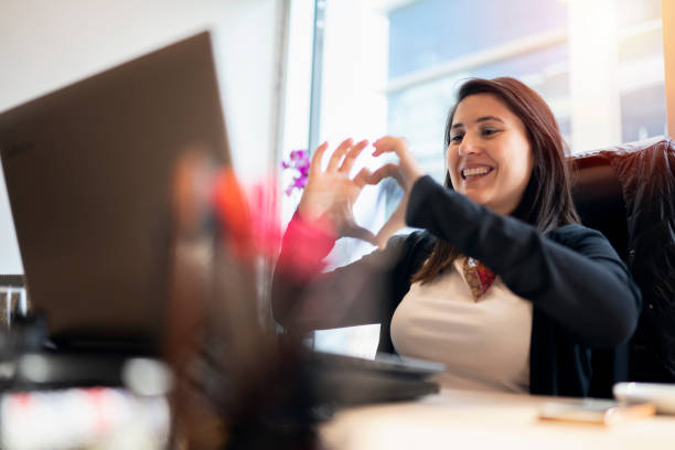 mujer en la oficina de video chat, y haciendo forma de corazón - happy valentines day fotografías e imágenes de stock