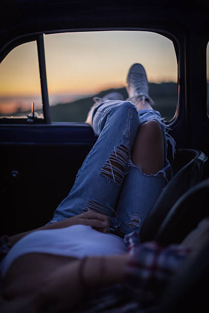 Woman at sunset with legs out of the car window stock photo