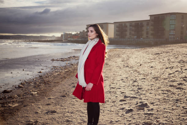 Woman at the beach, wearing a red jacket, showing expressions concerned with anxiety, stress, depression etc. stock photo