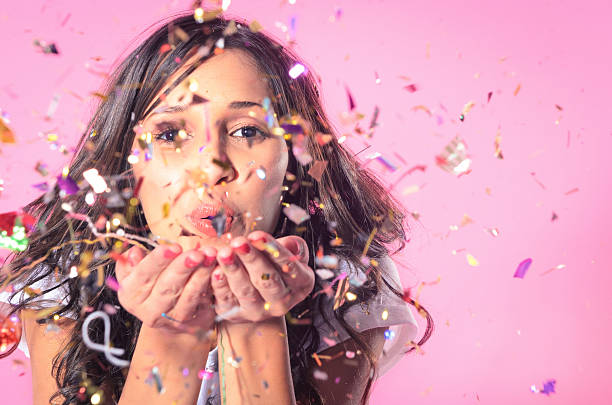 Woman blowing colourful confetti Portrait of beautiful woman blowing confetti in the air, party new years eve celebration on pink background new years eve girl stock pictures, royalty-free photos & images