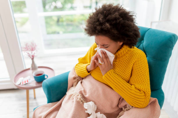 Woman blowing nose Portrait of sick woman sitting in an armchair covered with blanket, having a flu and fever, blowing nose into a paper tissue curley cup stock pictures, royalty-free photos & images