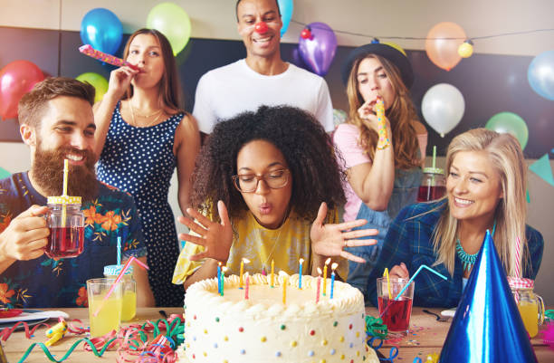 Woman blowing out candles on her cake Beautiful young adult woman blowing out candles on her cake at birthday party surrounded by celebrating friends happy birthday in danish stock pictures, royalty-free photos & images