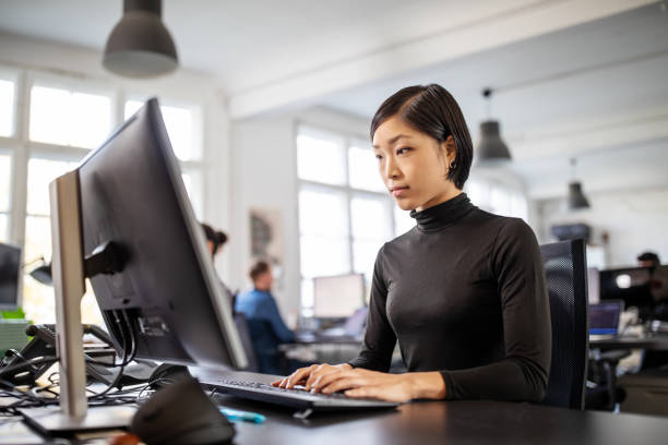 kvinna upptagen med att arbeta vid sitt skrivbord i öppen planlösning kontor - använda en dator bildbanksfoton och bilder