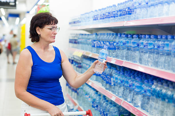 woman buys a bottle of water in the store - soda supermarket stockfoto's en -beelden