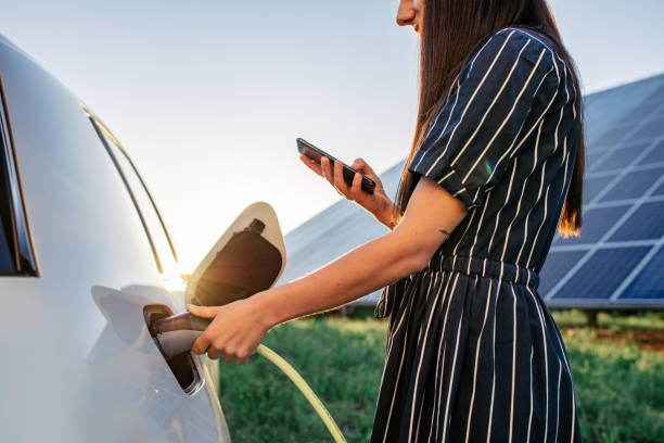 kvinna laddar elbil och solpaneler i bakgrunden - electric car woman bildbanksfoton och bilder
