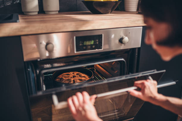 Woman checking apple pie in oven stock photo