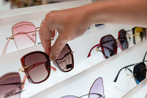 Close-up shot of female hands choosing sunglasses to buy in department store.