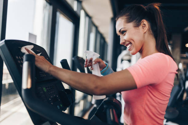 Woman cleaning fitness gym equipment Young happy and smiling woman cleaning and weeping expensive fitness gym equipment with sprayer and cloth. gym cleaning stock pictures, royalty-free photos & images