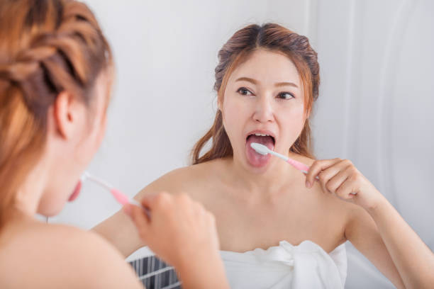 woman cleaning tongue using toothbrush with mirror in bathroom woman cleaning tongue using toothbrush with mirror in the bathroom healthy tongue picture stock pictures, royalty-free photos & images