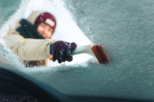Woman cleans windshield with ice scraper