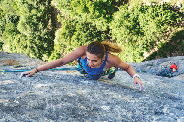 Woman climbs rock. Athletic beautiful blonde hair woman climbs a rock in the forest with rope. Sport climbing, lead. Upper view. rock face stock pictures, royalty-free photos & images