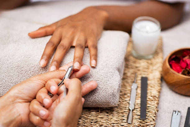 Woman clipping nails at salon Close up of manicurist hands clipping client nails in a luxury spa. Young woman getting manicure treatment with hands kept on towel. "rClipping nails, hand care and nailcare at beauty salon. nail salon stock pictures, royalty-free photos & images
