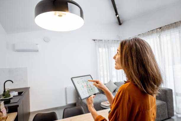 frau steuert licht mit einem digitalen tablet zu hause - smart home stock-fotos und bilder