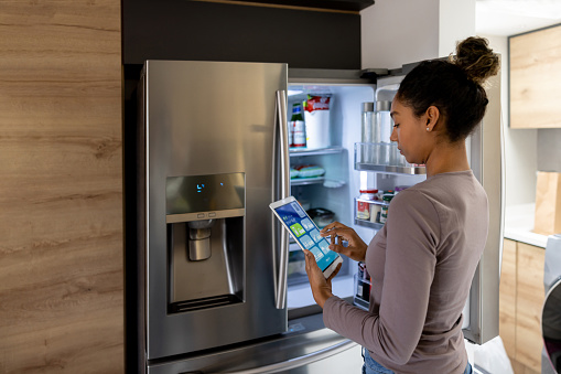 Woman controlling the fridge using an automated system from a tablet - smart home concepts. **DESIGN ON SCREEN WAS MADE FROM SCRATCH BY US**