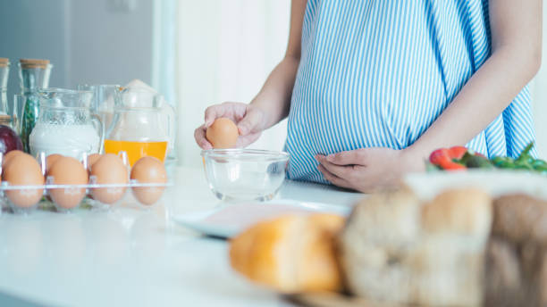 Woman cracking an egg into a bowl with  standing by in kitchen. Mother pregnant
cooking in kitchen. stock photo