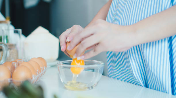 Woman cracking an egg into a bowl with  standing by in kitchen. Mother pregnant cooking in kitchen. stock photo