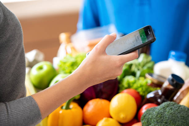 Woman customer checking grocery that ordered online via smarrt phone and just delivered by deliveryman at home, food delivery service concept stock photo
