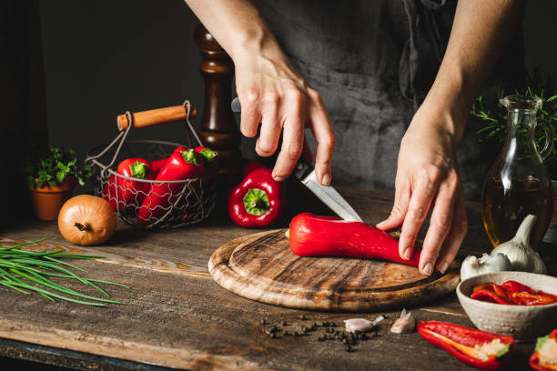 Woman cutting chili peppers to prepare red pepper soup Close-up of a woman hands cutting red peppers on a chopping board. Woman chef preparing red pepper soup in kitchen. pepper vegetable stock pictures, royalty-free photos & images