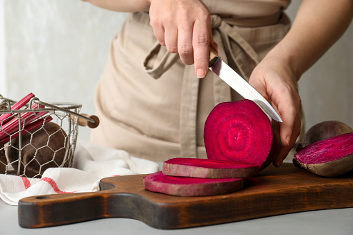 Woman cutting fresh red beet at table, closeup