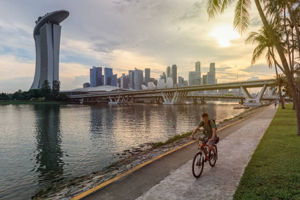 Woman cycling in down town in front of the Marina Bay Sands and Modern Art Museum at sunset stock photo