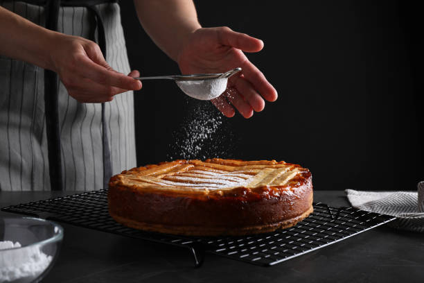Woman decorating tasty apricot pie with powdered sugar at black table, closeup Woman decorating tasty apricot pie with powdered sugar at black table, closeup confectioner stock pictures, royalty-free photos & images